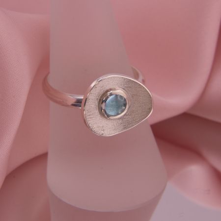 Präsentation des Rings Isola auf einem Schmuckständer zeigt die skulpturale Form und das Funkeln des blauen Edelsteins.